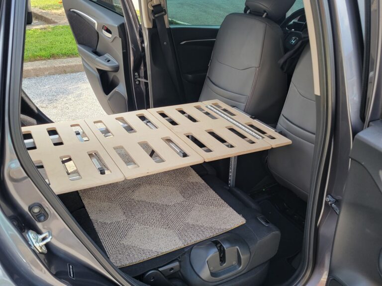 A Trunk Mate wooden slatted sleeping platform set up over a carpeted mat, fitted perfectly across the folded-down back seats of a car—turning your ride into a comfy place to crash.