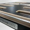 Close-up of a Trunk Mate platform showing off the layered plywood construction, durable textured black surface, elongated slots for ventilation or attachments, and sleek metal trim—built tough for adventure.