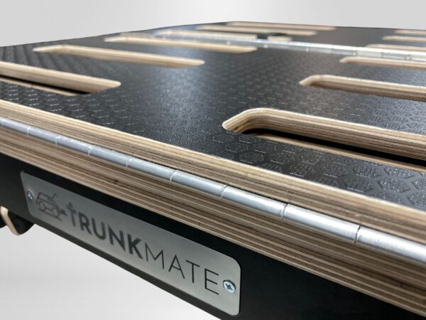 Close-up of a Trunk Mate platform showing off the layered plywood construction, durable textured black surface, elongated slots for ventilation or attachments, and sleek metal trim—built tough for adventure.