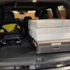 An SUV trunk with a folded child stroller on the left and two Trunk Mate Sleeping Platform mattresses stacked on a storage box on the right, showing roomy, organized cargo space for family adventures.