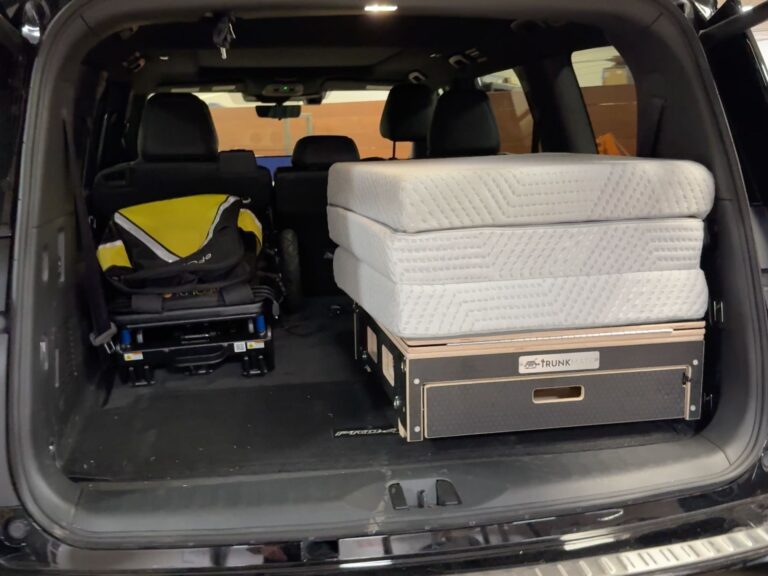 An SUV trunk with a folded child stroller on the left and two Trunk Mate Sleeping Platform mattresses stacked on a storage box on the right, showing roomy, organized cargo space for family adventures.