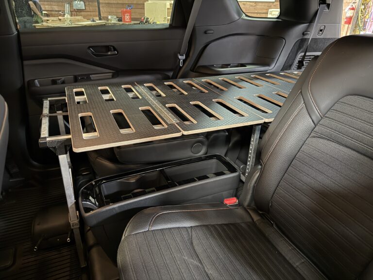 A sturdy Trunk Mate cargo shelf, made from metal and composite materials, is securely installed above the folded rear seats inside a vehicle—creating extra storage space right behind the front passenger area.