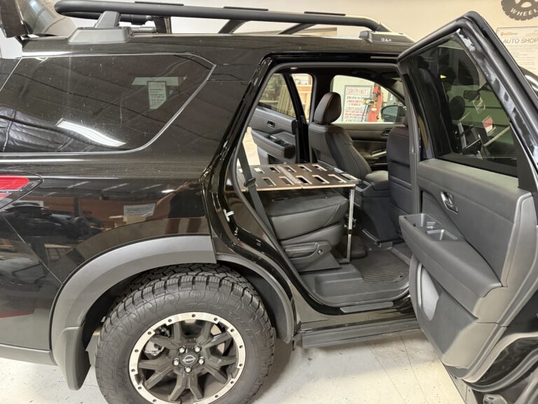 A black SUV with the rear passenger door open, showing off a Trunk Mate metal cargo platform installed securely over the folded back seat—ready for gear, groceries, or your next adventure.