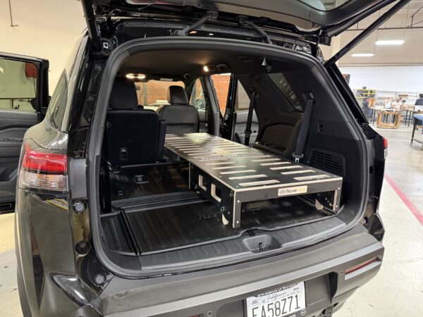 Custom wooden Trunk Mate sleeping platform set up in the open trunk of an SUV, with rear seats partially folded for extra room and organized storage underneath.