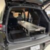 Custom wooden Trunk Mate sleeping platform set up in the open trunk of an SUV, with rear seats partially folded for extra room and organized storage underneath.