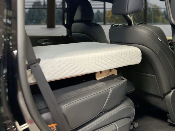 Trunk Mate Sleeping Platform set up in a car—mattress resting on a sturdy wooden base in the back seat area, front seat reclined and car door open for easy access.