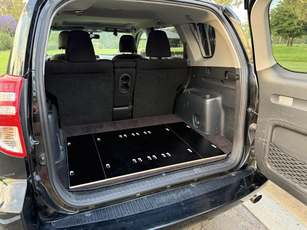 Rear view of an SUV with the tailgate open, featuring a Trunk Mate Sleeping Platform in sleek black—fits perfectly in the cargo area for organized storage and a comfy sleep setup.
