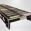 Trunk Mate sleeping platform with black and wood panels, handy rectangular cutouts, metal label, and sturdy legs against white.