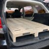 Trunk Mate wooden sleeping platform with ventilation slots set up in an SUV’s cargo space, rear seats folded flat and trunk open for easy car camping.