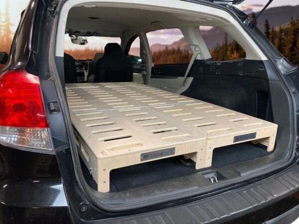 Trunk Mate wooden sleeping platform with ventilation slots set up in an SUV’s cargo space, rear seats folded flat and trunk open for easy car camping.
