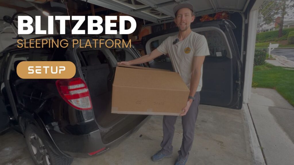 A man stands in a garage holding a cardboard box next to an open car trunk, getting ready to set up the BlitzBed Sleeping Platform—Trunk Mate’s easy, ready-to-go sleep solution for your next adventure. Text on the image says: "BLITZBED SLEEPING PLATFORM SETUP.