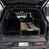 A spacious 2025 Nissan Pathfinder with its rear hatch open reveals a custom Trunk Mate Sleeping Platform—a sturdy mix of metal and wood—securely fitted in the cargo area, optimizing storage space and creating a flat sleeping surface for your next adventure.