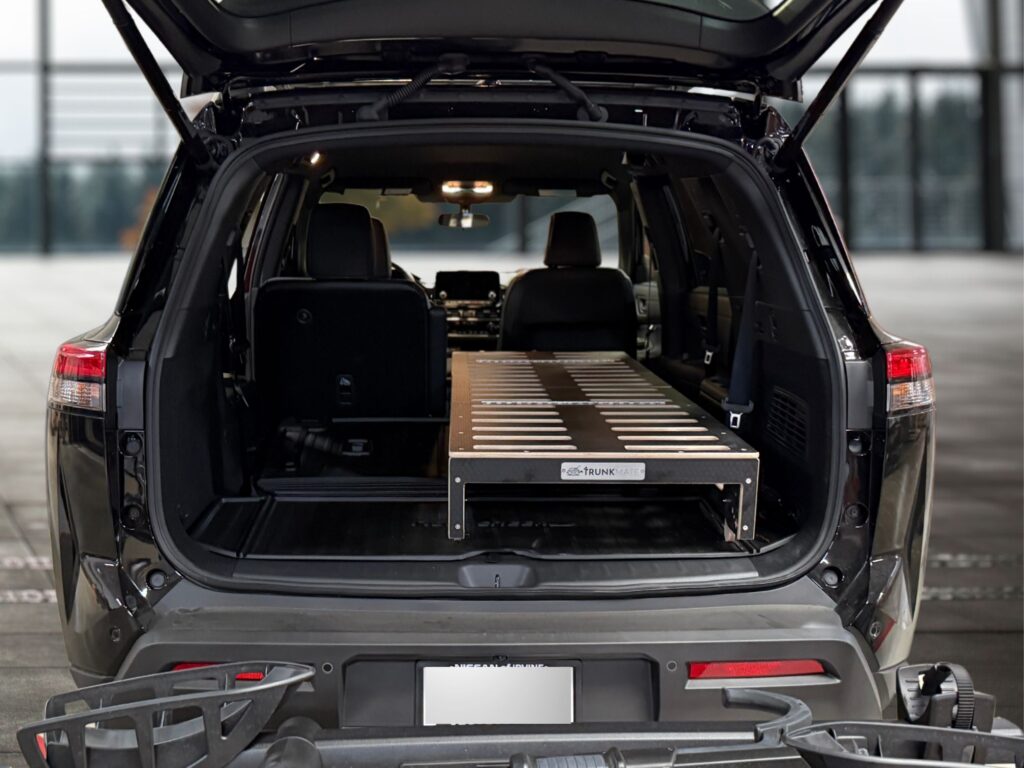 A spacious 2025 Nissan Pathfinder with its rear hatch open reveals a custom Trunk Mate Sleeping Platform—a sturdy mix of metal and wood—securely fitted in the cargo area, optimizing storage space and creating a flat sleeping surface for your next adventure.