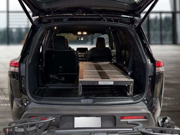 A spacious 2025 Nissan Pathfinder with its rear hatch open reveals a custom Trunk Mate Sleeping Platform—a sturdy mix of metal and wood—securely fitted in the cargo area, optimizing storage space and creating a flat sleeping surface for your next adventure.