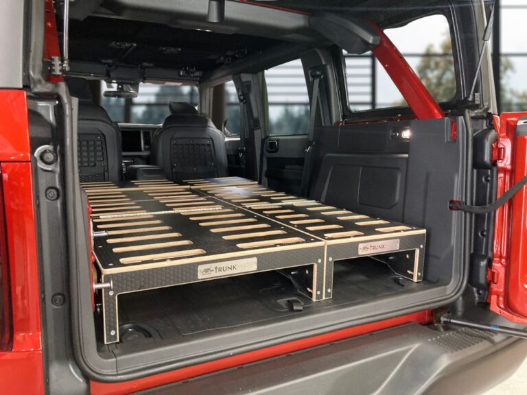 A red SUV with the back seats folded down and a Trunk Mate wooden sleeping platform fitted in the cargo space, ready for comfortable road trip sleeps or organized storage.