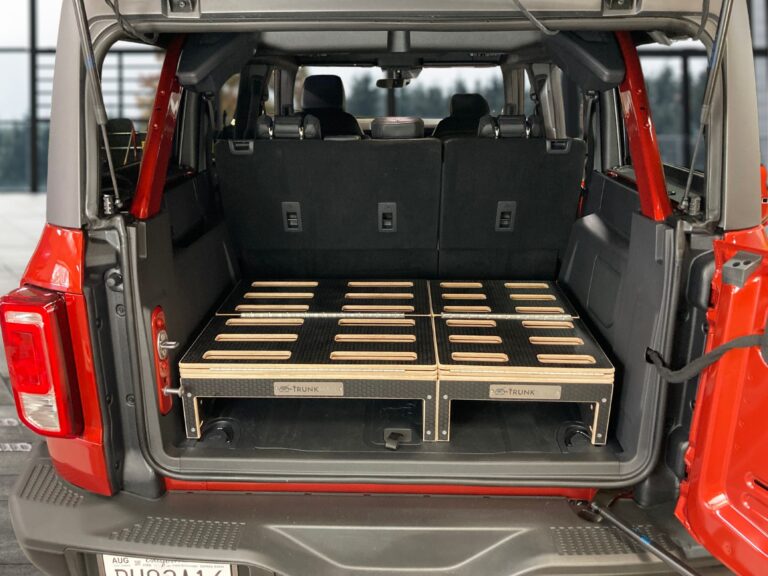 The open trunk of a red SUV reveals a Trunk Mate Sleeping Platform perfectly fitted in the cargo space, featuring custom cutouts for easy access and smart gear storage.