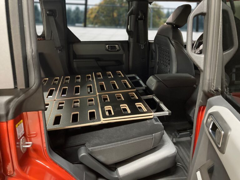 A Trunk Mate folding sleeping platform set up in a red car, transforming the space from the folded rear seats to the front seats into a flat, comfy surface for camping or road trips.