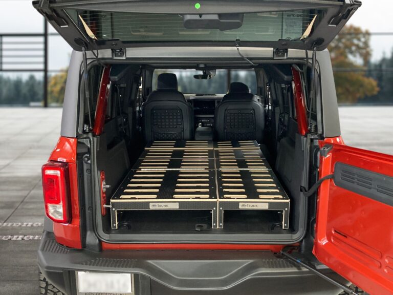 A red SUV with its trunk open, featuring a Trunk Mate custom wooden sleeping platform perfectly fitted in the cargo space—ready for camping or road trip adventures.