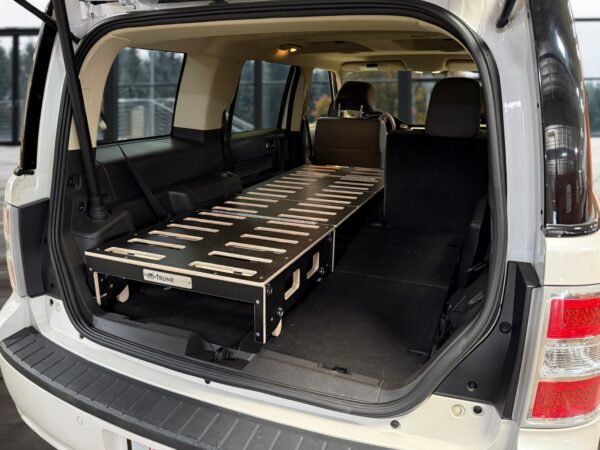 A sleek black and silver Trunk Mate sleeping platform set up in an SUV, showing off its modular design with the rear seats folded flat for plenty of sleeping space.
