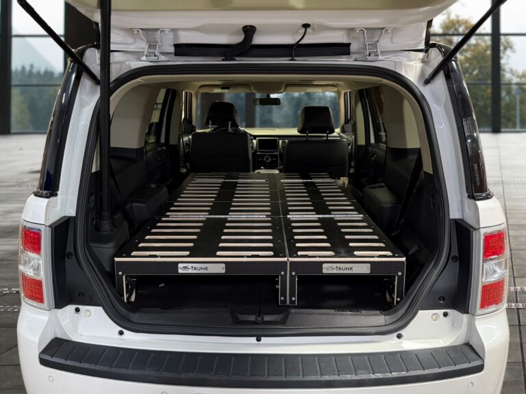 The back of an SUV with the hatch open, featuring a Trunk Mate sleeping platform stretched from the folded seats to the cargo space—ready for comfortable car camping and easy storage underneath.