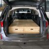 Trunk Mate sleeping platform installed in a minivan, hatch open to reveal spacious wooden drawers for organized storage.
