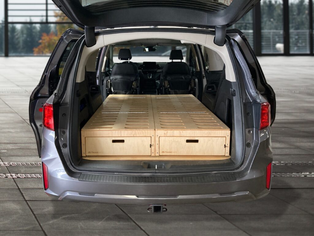 Trunk Mate sleeping platform installed in a minivan, hatch open to reveal spacious wooden drawers for organized storage.