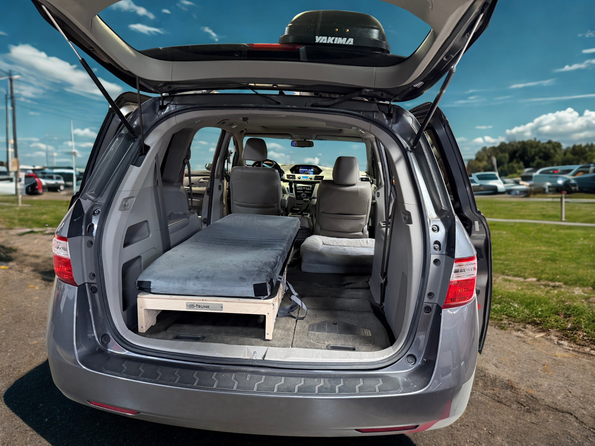 The back of a minivan open, showing a Trunk Mate sleeping platform with mattress, ready for camping or road trip adventures.