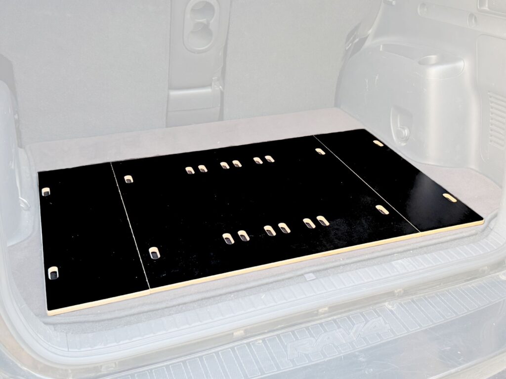 A black Trunk Mate Sleeping Platform with versatile cutouts lays flat in a vehicle’s cargo area, ready for a comfy night’s rest or gear organization.