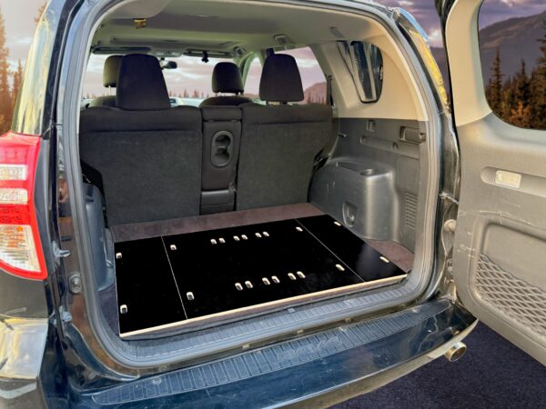 SUV cargo area fitted with a Trunk Mate black storage platform; back seats remain upright, creating organized trunk space with scenic mountains in the background.